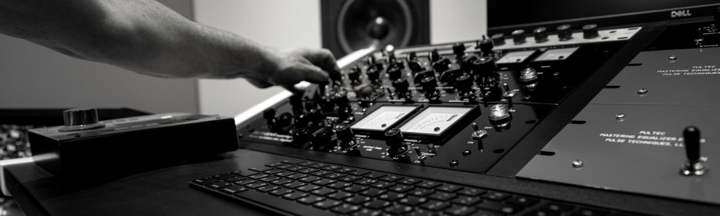 Eine Hand bedient ein großes Mischpult zur Musikproduktion.